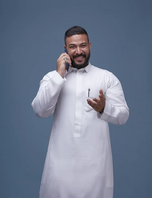 رجل سعودي بالثوب الأبيض التقليدي يتحدث عبر الهاتف الذكي