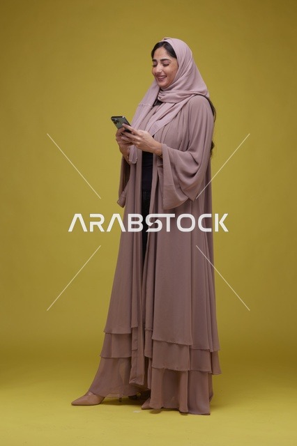 امرأة سعودية تستخدم الهاتف الذكي بخلفية استوديو صفراء