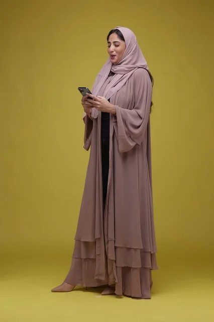 Saudi Woman Using Smartphone on Yellow Studio Background