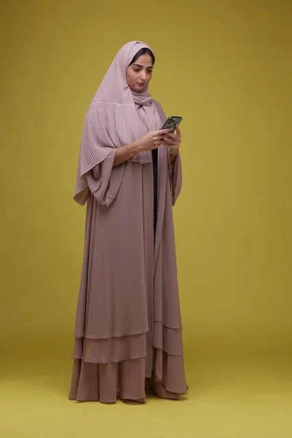 امرأة سعودية تستخدم الهاتف الذكي في استوديو بخلفية صفراء