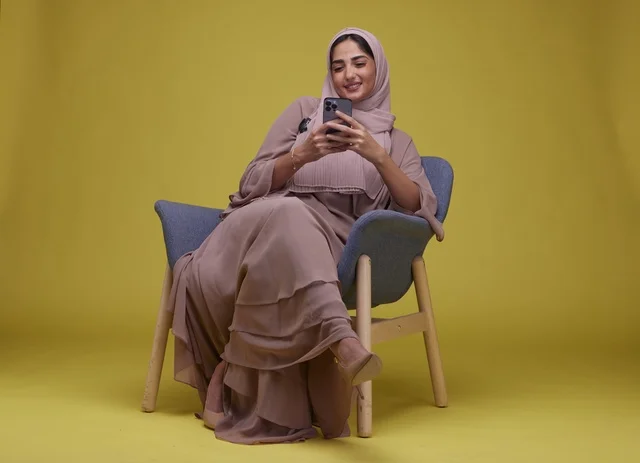 امرأة سعودية في استوديو تستخدم هاتف ذكي بخلفية صفراء