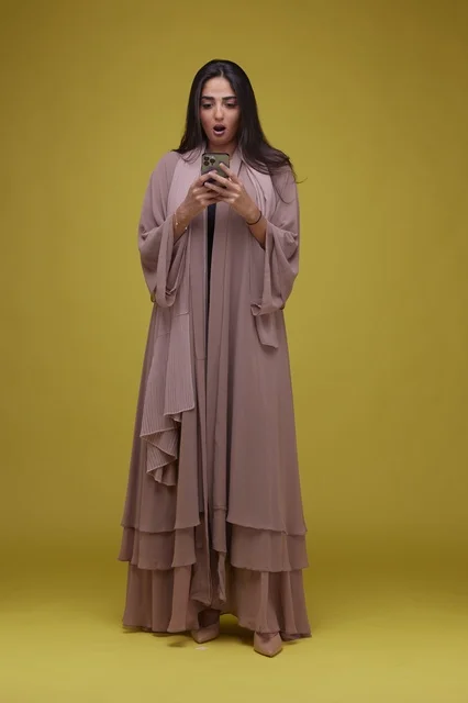 Surprised Saudi Woman Using Smartphone on Yellow Background