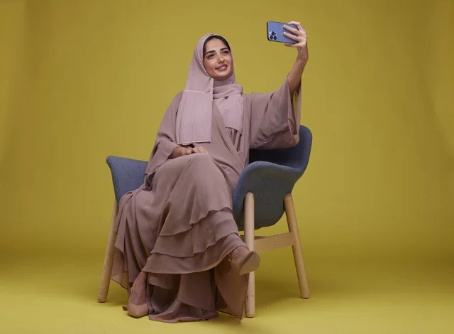 امرأة سعودية تلتقط صورة سيلفي أمام خلفية صفراء