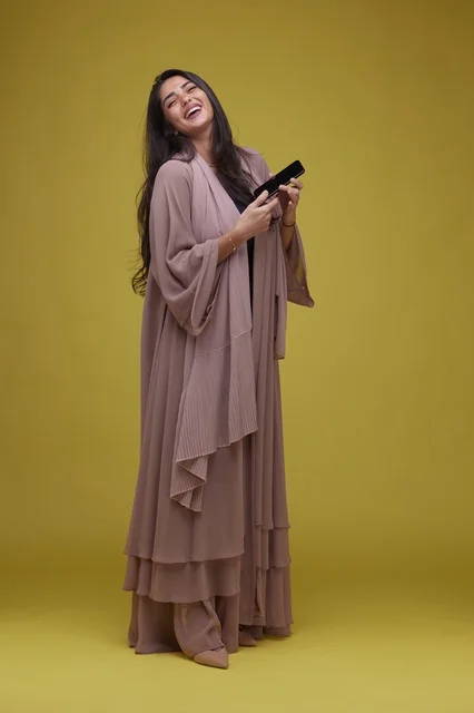 Saudi Woman in Abaya Holding Phone on Yellow Background