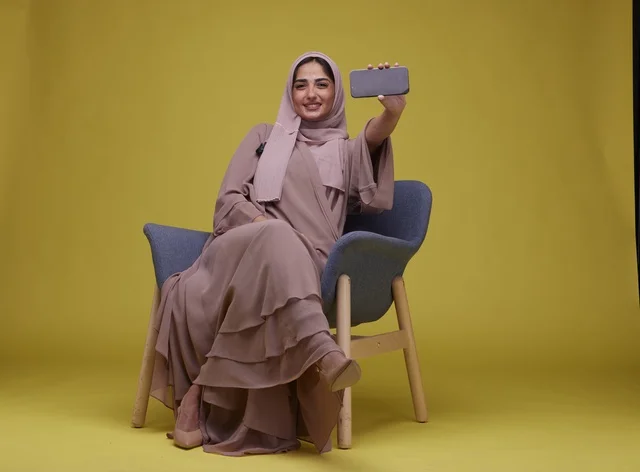 امرأة سعودية تحمل هاتف ذكي بخلفية صفراء امرأة سعودية تحمل هاتف ذكي بخلفية صفراء