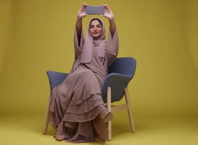امرأة سعودية مع هاتف ذكي بخلفية صفراء