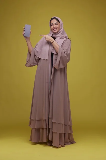 امرأة سعودية مبتسمة تحمل هاتف ذكي بشاشة فارغة