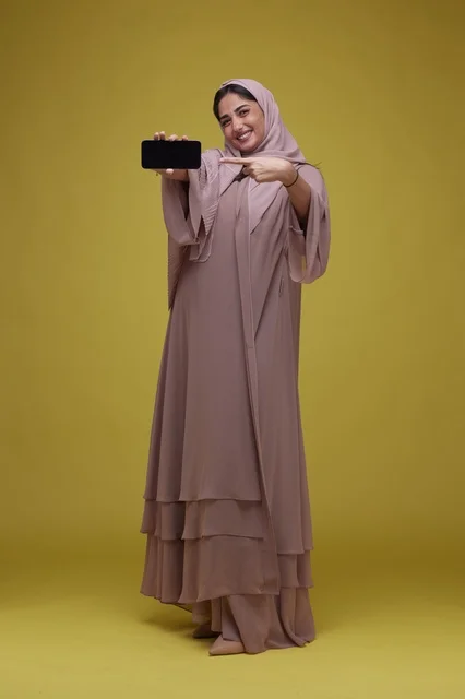 Smiling Saudi Woman Holding Smartphone on Yellow Background