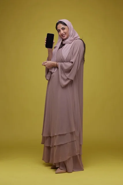 امرأة سعودية تحمل هاتف ذكي بشاشة فارغة خلفية صفراء