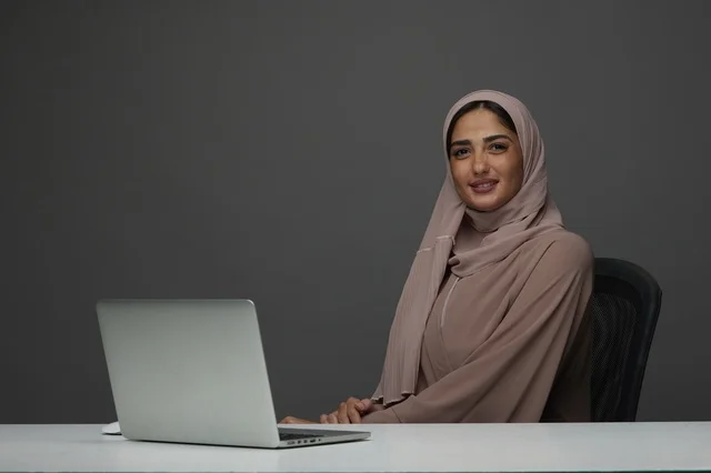 سيدة أعمال سعودية مبتسمة مع كمبيوتر محمول على المكتب سيدة أعمال سعودية مبتسمة مع كمبيوتر محمول على المكتب