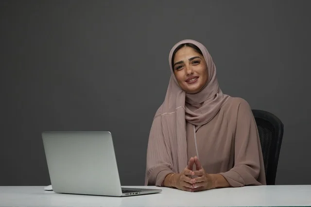Smiling Saudi Businesswoman at Desk Interacting with Camera