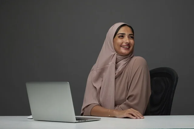 سيدة أعمال سعودية مبتسمة مع لابتوب في المكتب