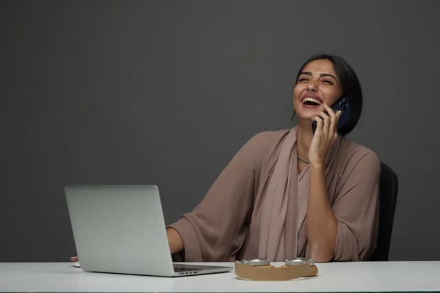 Saudi Businesswoman Laughing During Phone Call at Desk