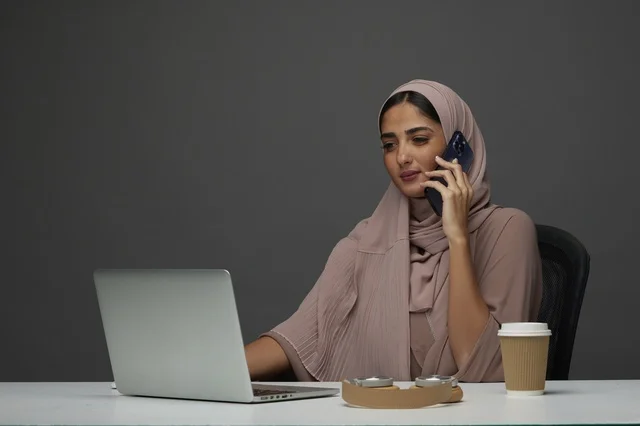 سيدة أعمال سعودية تجري مكالمة هاتفية مع لابتوب على المكتب