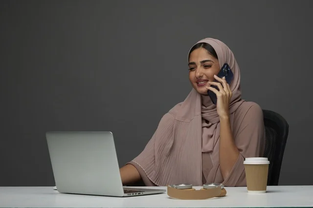 سيدة أعمال سعودية تتحدث بالهاتف مع لابتوب في المكتب