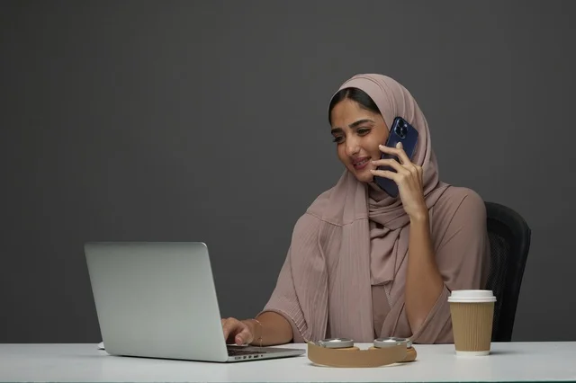 سيدة أعمال سعودية تجري مكالمة هاتفية مع لابتوب بالمكتب