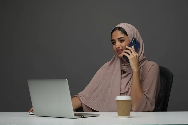 Saudi Businesswoman Making Phone Call with Laptop at Desk
