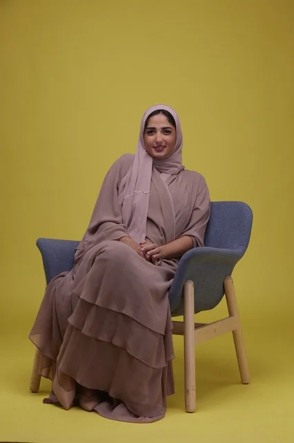 امرأة سعودية بالعباءة أمام خلفية صفراء