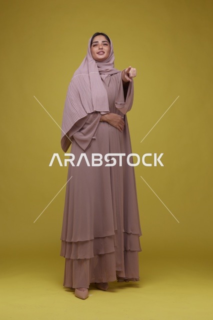 Saudi Woman in Pink Abaya Pointing on Yellow Background - Photo