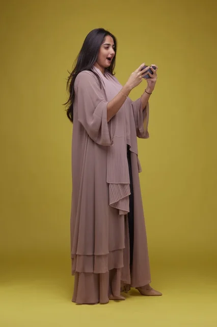 Young Saudi Woman Playing Mobile Game on Yellow Background