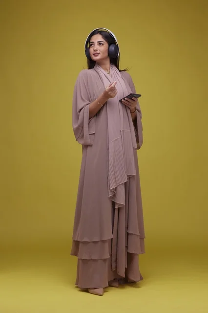Saudi Woman with Headphones and Smartphone on Yellow Background