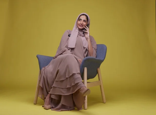 Saudi Woman Talking on Smartphone in Armchair Yellow Background