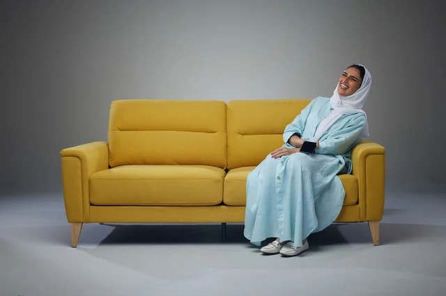 امرأة سعودية على أريكة صفراء مع هاتف ذكي