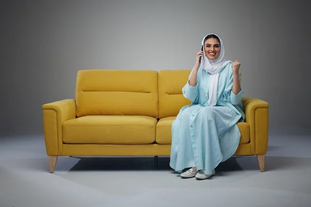 امرأة سعودية تتحدث عبر الهاتف الذكي على أريكة صفراء