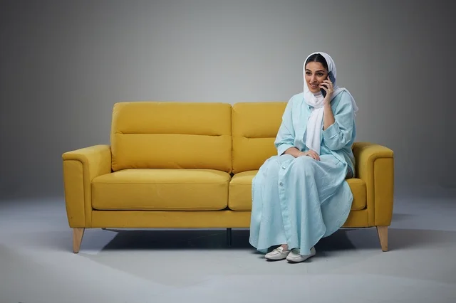 Saudi Woman Talking on Smartphone Sitting on Yellow Sofa