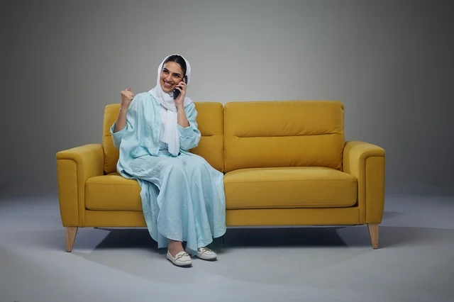 امرأة سعودية على أريكة صفراء تتحدث عبر الهاتف الذكي