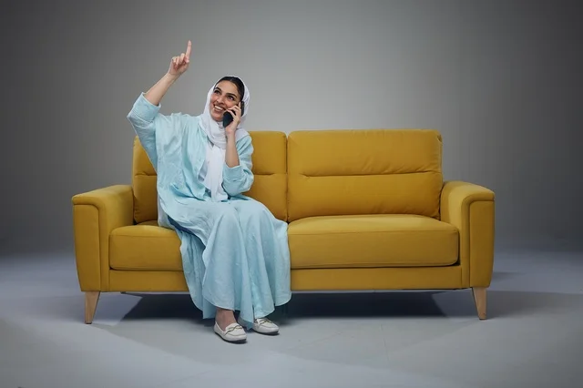 Saudi Woman on Yellow Sofa Talking on Smartphone Studio