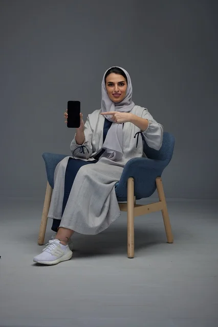 امرأة سعودية بعباية تشير إلى هاتف ذكي في الاستوديو