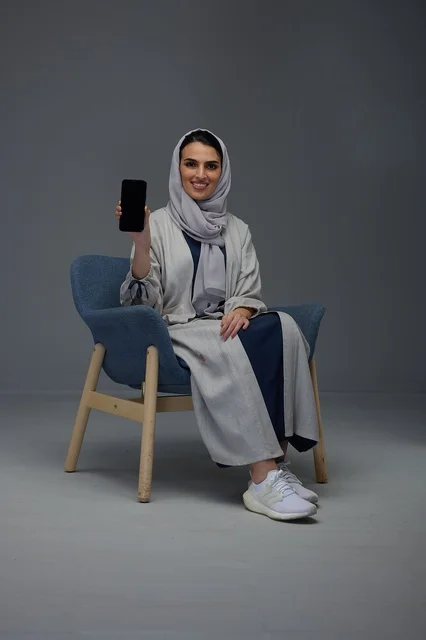 Saudi Woman Holding Smartphone Toward Camera in Studio