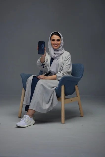 امرأة سعودية تجلس على كرسي أزرق وتحمل هاتفاً ذكياً