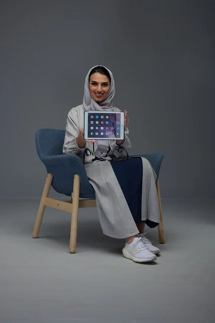 امرأة سعودية تحمل جهازاً لوحياً وتجلس على كرسي