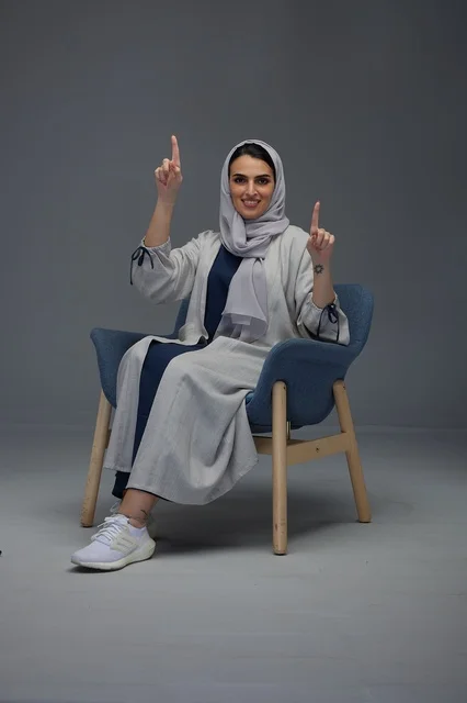 امرأة سعودية بالعباية الرمادية تشير للأعلى في الاستوديو