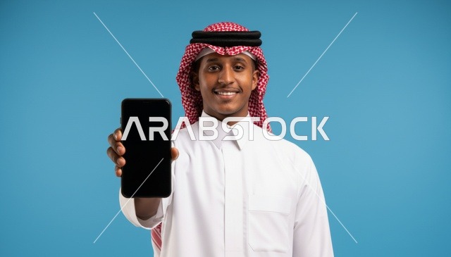 رجل سعودي يرتدي الثوب التقليدي يحمل هاتف ذكي بخلفية زرقاء