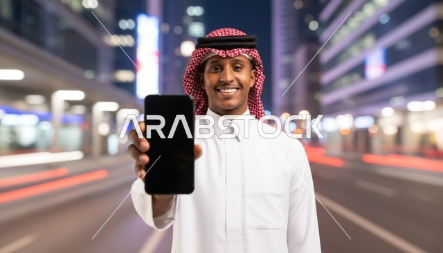 رجل سعودي يحمل هاتفاً ذكياً بشاشة فارغة ليلاً