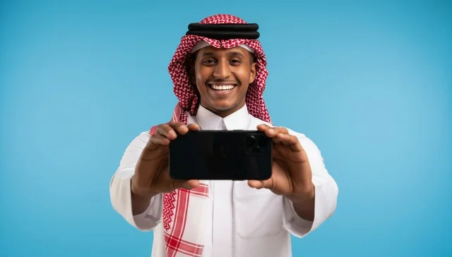 رجل سعودي بالزي التقليدي يمسك هاتفاً ذكياً