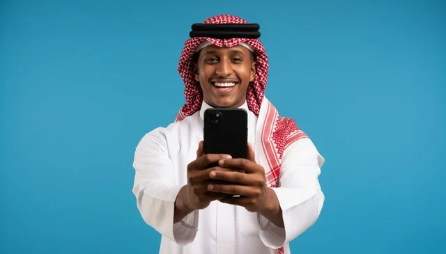 شاب سعودي بالثوب التقليدي يمسك هاتفاً ذكياً