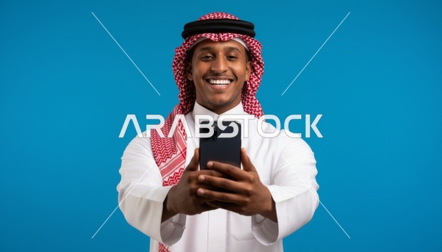 رجل سعودي مبتسم يحمل هاتف ذكي أمام خلفية زرقاء