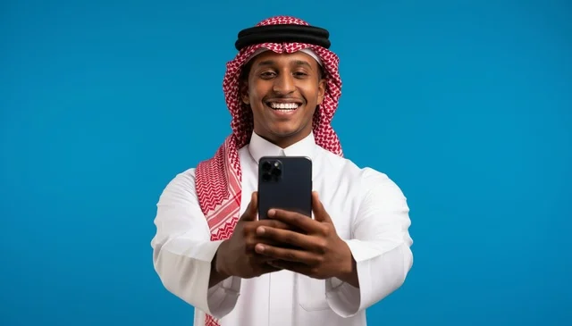 رجل سعودي مبتسم يحمل هاتف ذكي أمام خلفية زرقاء