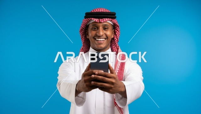 رجل سعودي مبتسم يحمل هاتف ذكي أمام خلفية زرقاء