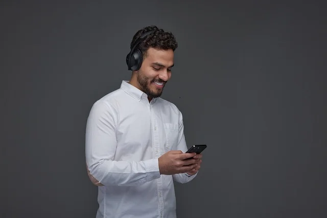 رجل سعودي يستخدم الهاتف مع سماعات الرأس بخلفية رمادية
