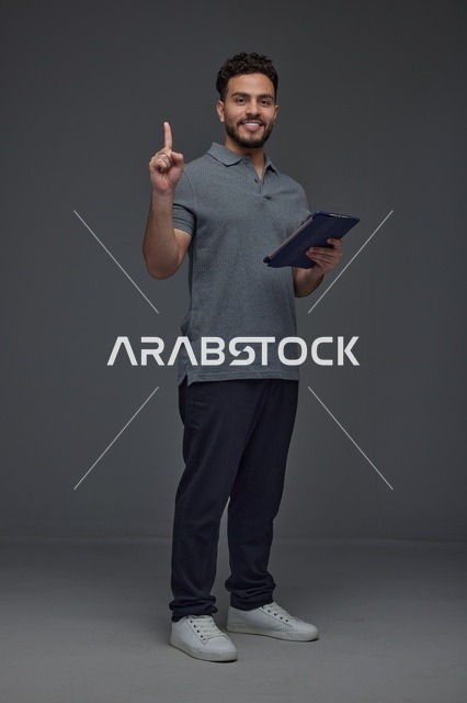 رجل سعودي يحمل جهازا لوحيا ويشير للأعلى في استوديو