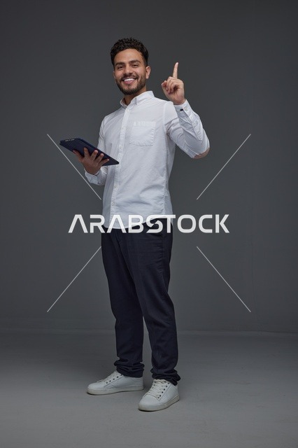 Saudi Man with Tablet Pointing Up on Grey Background