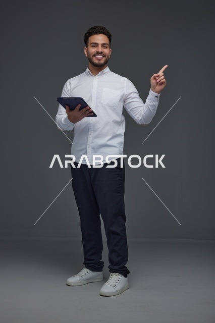 Man Holding Tablet and Pointing Upward on Grey Background