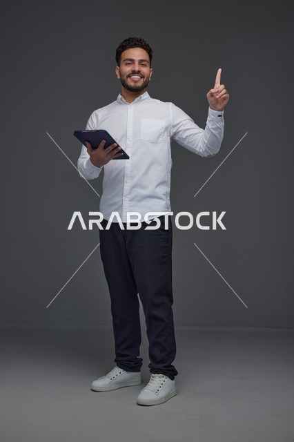 رجل سعودي مبتسم يحمل جهازاً لوحياً رقمياً ويشير للأعلى