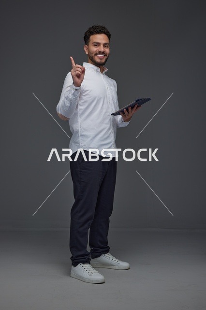 Saudi Man with Tablet Pointing Up on Gray Background