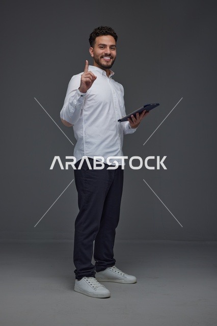 Saudi Man with Tablet Pointing Up on Gray Background